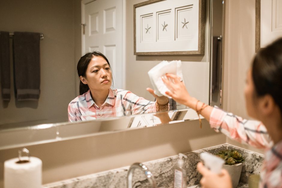 Focused woman cleaning a bathroom mirror, reflecting dedication to house chores.