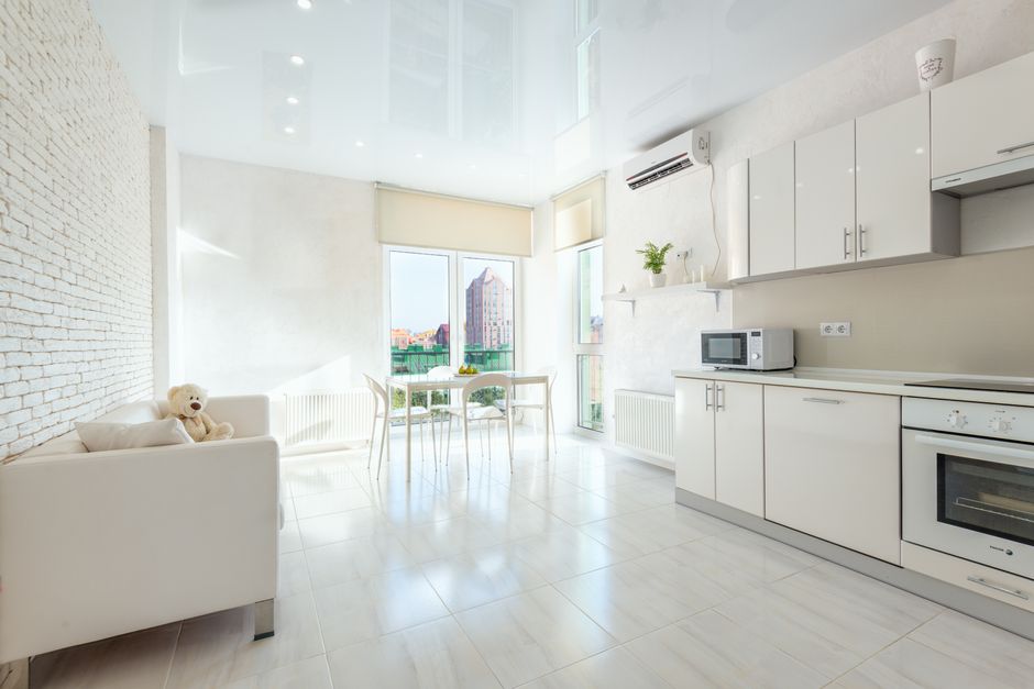 Interior of modern kitchen with appliances and dining table near balcony doors and couch under stretch ceiling